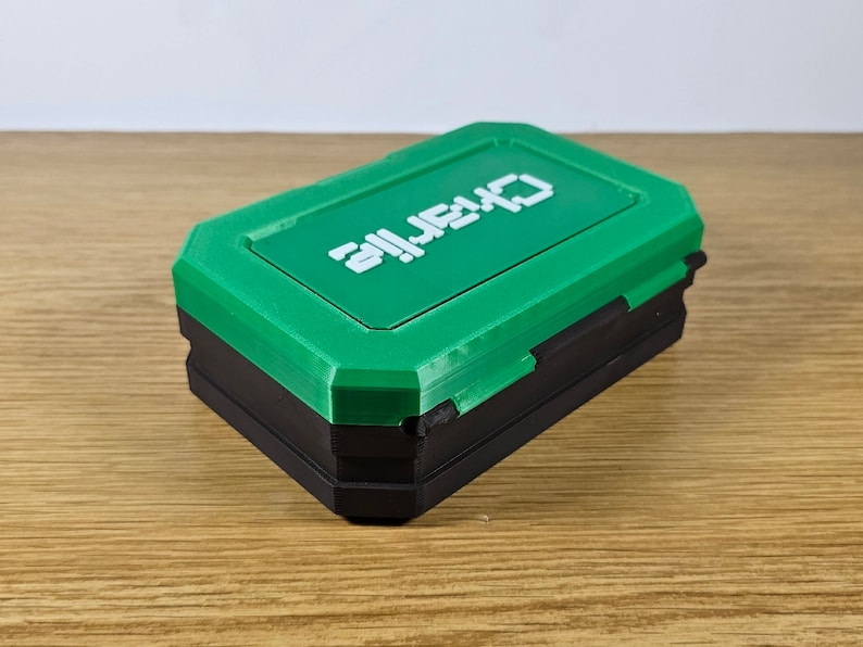 May include: A small, green and black box with the word "ALIEN" printed on the top. The box is made of plastic and has a hinged lid.
