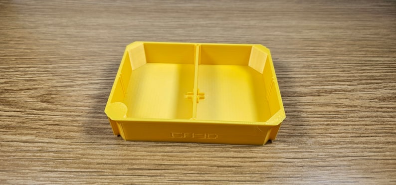 May include: A yellow plastic tray with two compartments. The tray has a raised edge around the perimeter and a small divider in the middle.