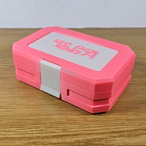 May include: A pink plastic storage box with a white lid. The lid has the word "AGSP" embossed on it.