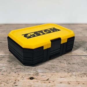 May include: A yellow and black storage box with the word "CUSTOM" printed on the top. The box has a rectangular shape and is made of plastic. The box is sitting on a wooden surface.