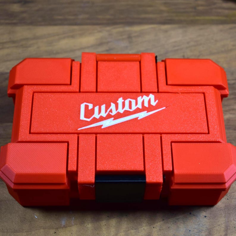 May include: A red, rectangular tool case with the word "Custom" in white script and a lightning bolt design. The case has a handle and multiple compartments, and is made of a durable plastic material.