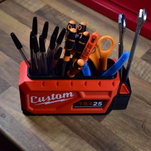 May include: A red and black tool organizer with the word "Custom" and the numbers "1S425" printed on the front. The organizer holds various tools, including pens, screwdrivers, scissors, and wrenches.