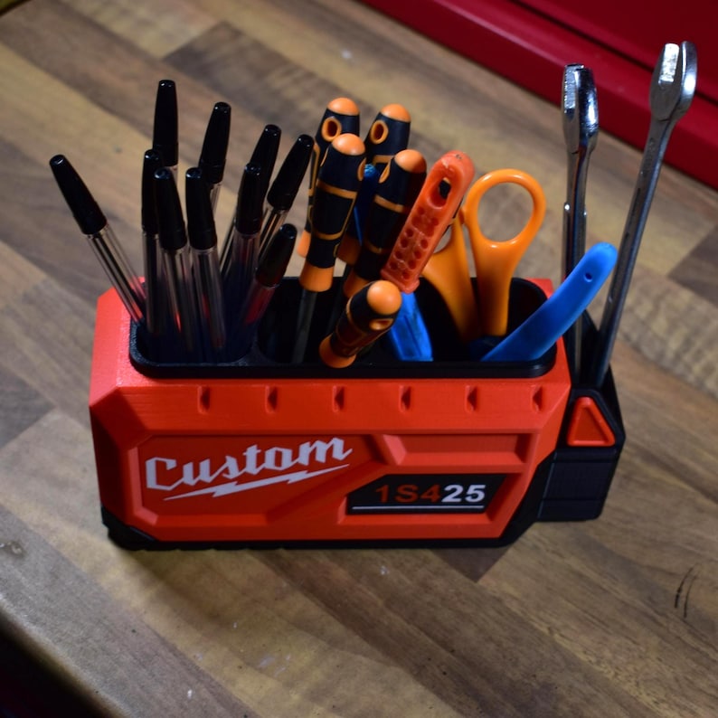 May include: A red and black tool organizer with the word "Custom" and the numbers "1S425" printed on the front. The organizer holds various tools, including pens, screwdrivers, scissors, and wrenches.