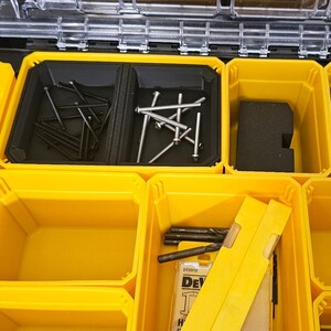 May include: Yellow plastic storage box with multiple compartments. The compartments contain various small hardware items, including screws, nails, and drill bits. The box is labeled "DeWalt" and has a model number.