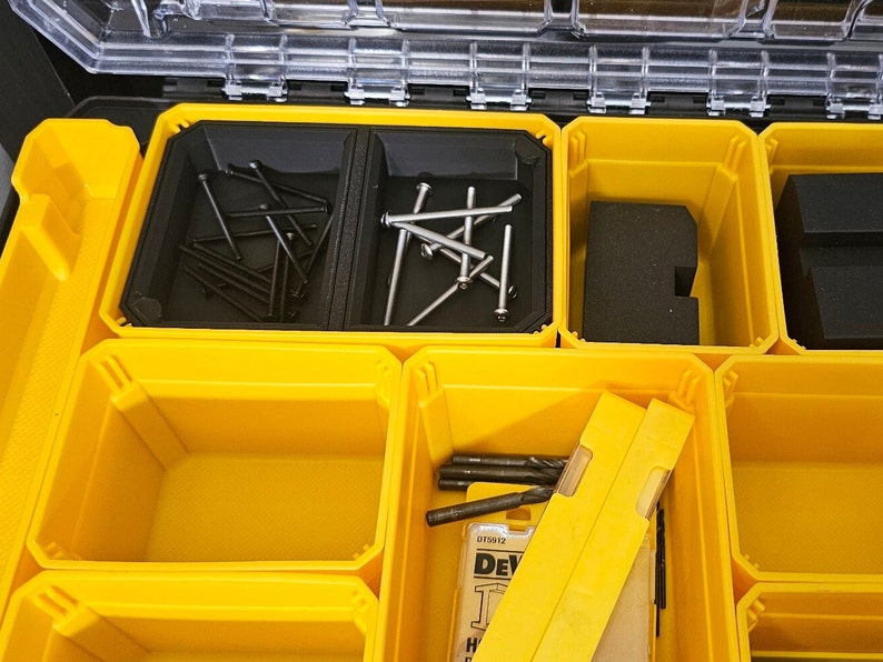 May include: Yellow plastic storage box with multiple compartments. The compartments contain various small hardware items, including screws, nails, and drill bits. The box is labeled "DeWalt" and has a model number.