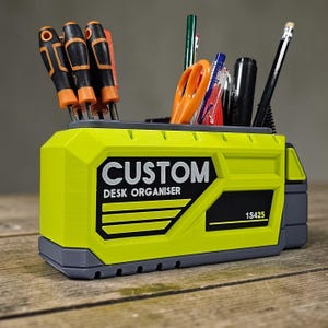 May include: A custom desk organizer in a bright yellow and gray color scheme, holding various tools and stationery. The organizer features the text "CUSTOM DESK ORGANISER" and the number "1S425". Screwdrivers, scissors, pens, and pencils are visible.
