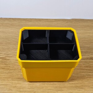 Puede incluir: Un organizador amarillo y negro con cuatro compartimentos. El exterior es de color amarillo brillante, mientras que los divisores interiores y la base son negros. El organizador est&aacute; dise&ntilde;ado con una forma geom&eacute;trica y parece ser de pl&aacute;stico.
