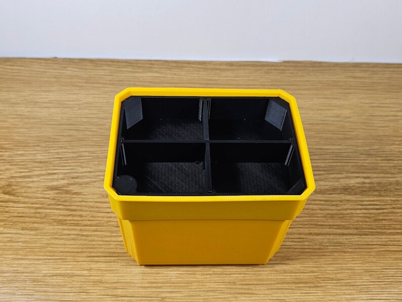 Puede incluir: Un organizador amarillo y negro con cuatro compartimentos. El exterior es de color amarillo brillante, mientras que los divisores interiores y la base son negros. El organizador est&aacute; dise&ntilde;ado con una forma geom&eacute;trica y parece ser de pl&aacute;stico.