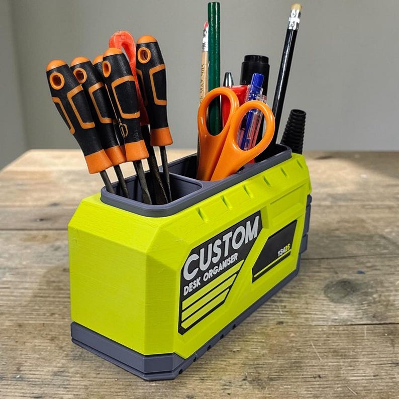 May include: A lime green desk organizer with the text "CUSTOM DESK ORGANISER" and a black and gray trim. The organizer holds screwdrivers, scissors, pencils, and pens. The organizer is made of plastic.