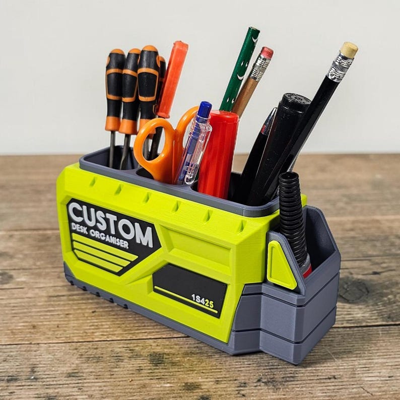May include: A custom desk organizer in a bright yellow and gray color scheme, filled with various office supplies. The organizer has the words "CUSTOM DESK ORGANISER" printed on the side, along with the number "18425". It holds screwdrivers, scissors, pens, and pencils.