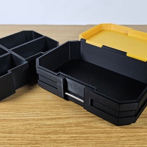May include: Two plastic storage boxes, one black with multiple compartments and one yellow with a lid. The black box is open and the yellow lid is off.