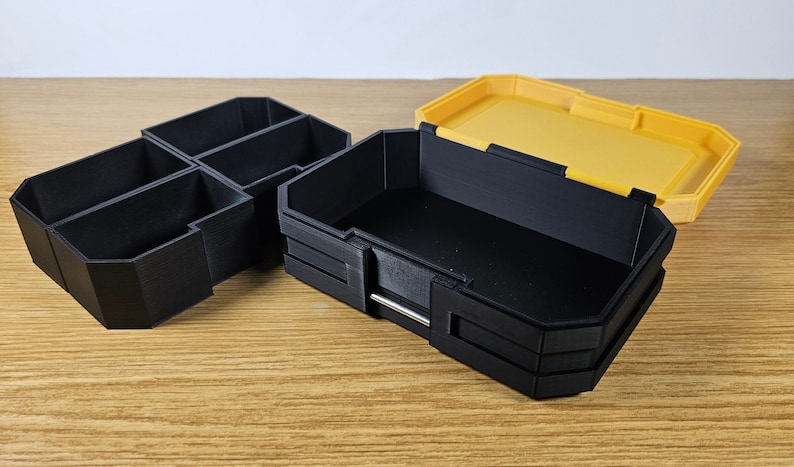 May include: Two plastic storage boxes, one black with multiple compartments and one yellow with a lid. The black box is open and the yellow lid is off.