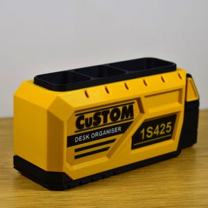 K&ouml;nnte beinhalten: Ein gelb-schwarzer Schreibtisch-Organizer mit dem Wort "CUSTOM" und "DESK ORGANISER" auf der Seite. Der Organizer hat drei F&auml;cher oben und die Nummer "1S425" ist auf der Seite aufgedruckt.