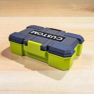 Peut inclure: Une bo&icirc;te de rangement vert citron et grise avec le mot "CUSTOM" imprim&eacute; sur le couvercle. La bo&icirc;te a une forme rectangulaire avec un couvercle &agrave; charni&egrave;re et est pos&eacute;e sur une surface en bois.