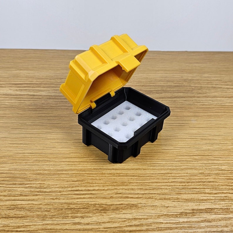May include: A small yellow and black plastic storage case with a hinged lid. The case has a foam insert with multiple compartments.