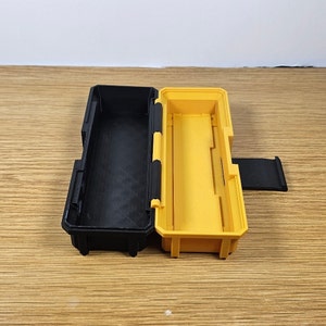 K&ouml;nnte beinhalten: Eine schwarze und gelbe Aufbewahrungsbox aus Kunststoff mit einem Scharnierdeckel. Die Box ist ge&ouml;ffnet und das Innere ist sichtbar.