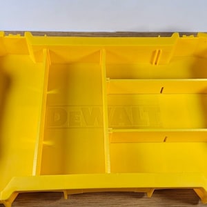 Op de afbeelding: Gele kunststofffen opbergdoos met verdelers en het DEWALT-logo. De doos maakt deel uit van het TOUGHSYSTEM.