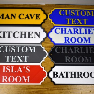 Puede incluir: Colecci&oacute;n de letreros decorativos para habitaciones en varios colores, incluyendo amarillo, azul, negro, rojo y blanco. Cada letrero presenta texto personalizado como "Man Cave", "Kitchen" y "Bathroom".