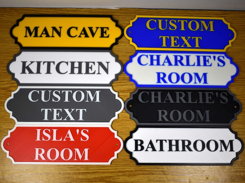 Puede incluir: Colecci&oacute;n de letreros decorativos para habitaciones en varios colores, incluyendo amarillo, azul, negro, rojo y blanco. Cada letrero presenta texto personalizado como "Man Cave", "Kitchen" y "Bathroom".