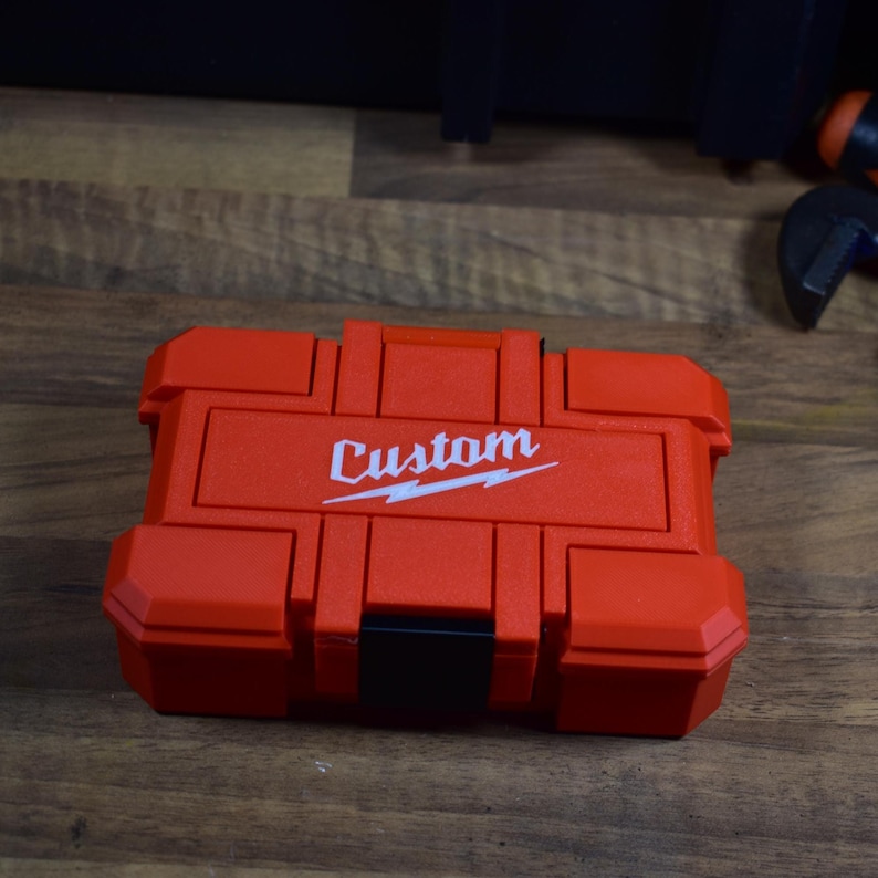 May include: A red tool case with the word "Custom" printed in white. The case has a black latch and is made of a durable material. The case is designed to hold tools and other small items.