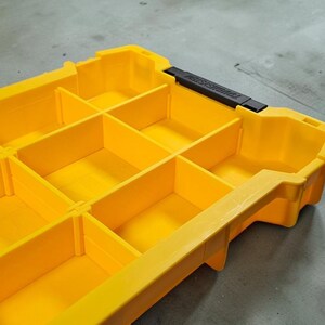 May include: A yellow plastic parts organiser with multiple compartments. The container has a black handle and is designed for storing small items. The compartments are divided by vertical and horizontal dividers.