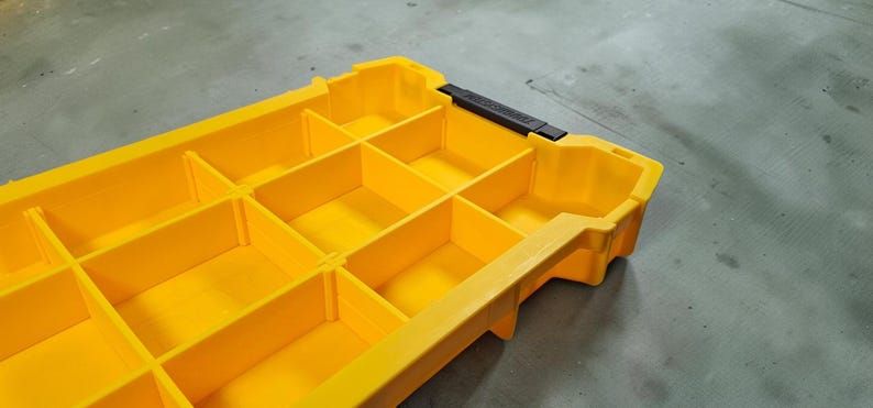May include: A yellow plastic parts organiser with multiple compartments. The container has a black handle and is designed for storing small items. The compartments are divided by vertical and horizontal dividers.