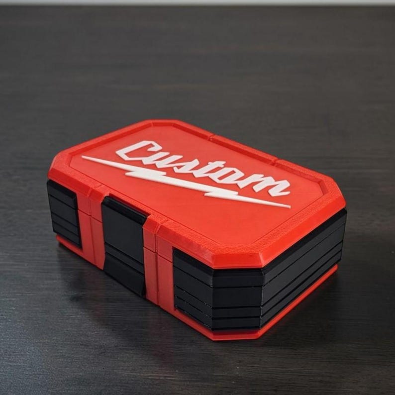 May include: A red and black rectangular box with the word "Custom" in white script and a white lightning bolt design. The box has a layered design and is on a dark surface.