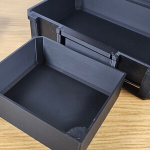 May include: A black plastic storage box with a removable tray. The box is open and the tray is pulled out, revealing the empty interior.