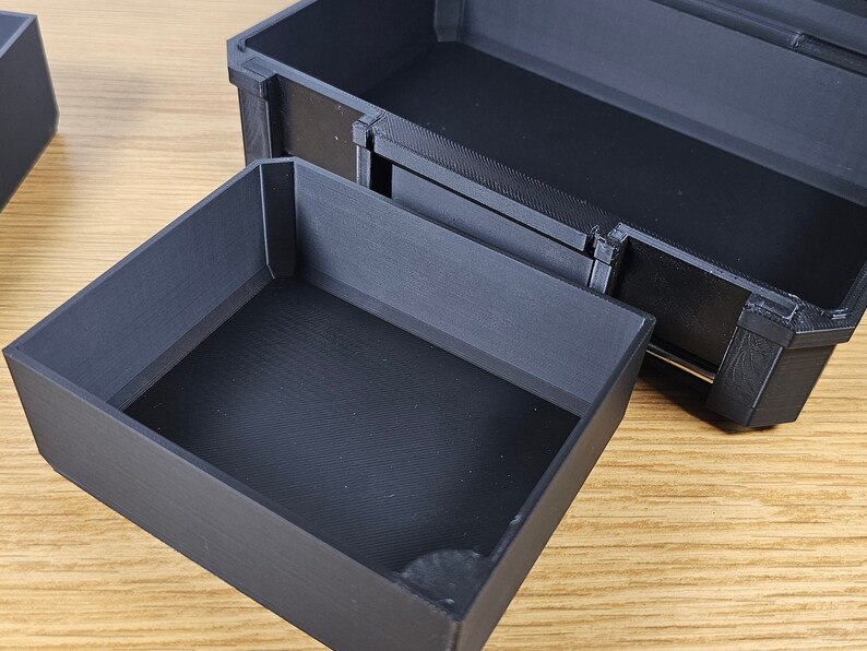May include: A black plastic storage box with a removable tray. The box is open and the tray is pulled out, revealing the empty interior.