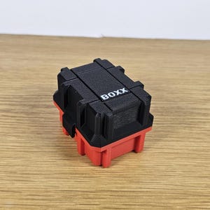 Pu&ograve; includere: Una piccola scatola di immagazzinaggio nera e rossa con la parola "BOXX" stampata sulla parte superiore.