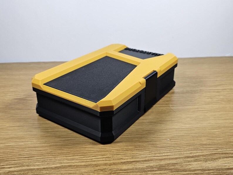 May include: A black and yellow plastic storage box with a textured lid. The box is closed and sitting on a wooden surface.