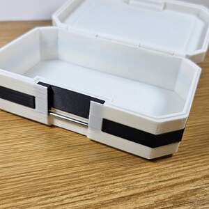Puede incluir: Una caja de almacenamiento de pl&aacute;stico blanco con un borde negro alrededor de los bordes. La caja est&aacute; abierta y vac&iacute;a.