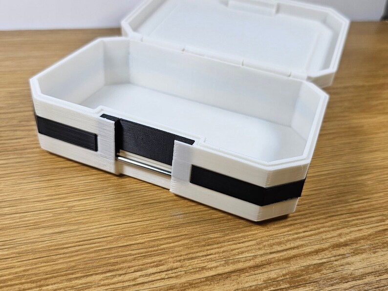 Puede incluir: Una caja de almacenamiento de pl&aacute;stico blanco con un borde negro alrededor de los bordes. La caja est&aacute; abierta y vac&iacute;a.