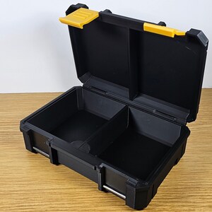 May include: A black plastic storage box with a yellow latch. The box has two compartments inside.