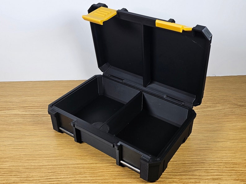 May include: A black plastic storage box with a yellow latch. The box has two compartments inside.