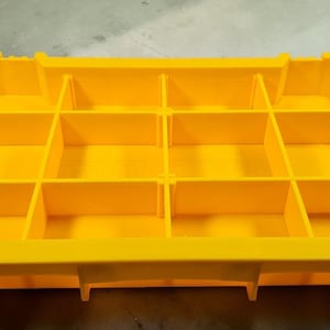 May include: A yellow parts organiser with multiple compartments. The organiser has a rectangular shape with black handles on each end. The interior is divided into several sections, ideal for storing small items like screws or hardware.