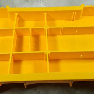 May include: Bright yellow plastic organizer with multiple compartments. The organizer has black handles on each side with the text "TOUGH SYSTEM". The compartments are divided by vertical and horizontal dividers.