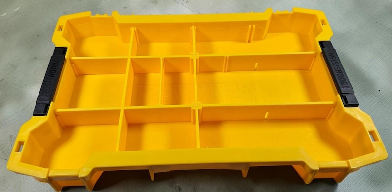 May include: Bright yellow plastic organizer with multiple compartments. The organizer has black handles on each side with the text "TOUGH SYSTEM". The compartments are divided by vertical and horizontal dividers.