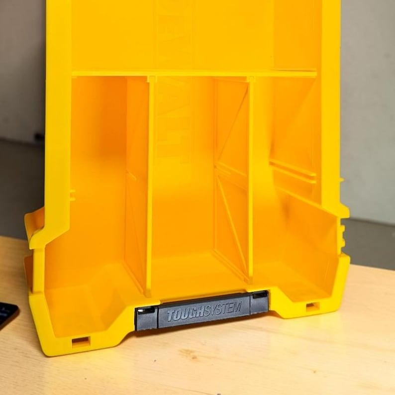 May include: A bright yellow plastic storage organizer featuring three vertical compartments separated by internal dividers. The front edge includes a black horizontal latch handle with the embossed text TOUGHSYSTEM in capital letters.
