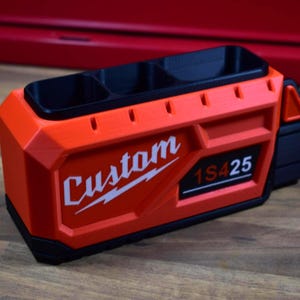 May include: An orange and black custom-made tool organizer with three compartments. The organizer has the word "Custom" in white lettering and the numbers "1S425" on the side. The tool organizer is designed to hold tools.