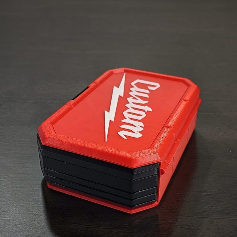 May include: A red and black rectangular box. The lid features the word "Custom" and a white lightning bolt graphic. The box has a textured surface and a hinged design.