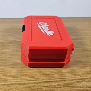 May include: A red tool box with the word "Charlie" printed in white on the top. The box is closed and has a black latch.