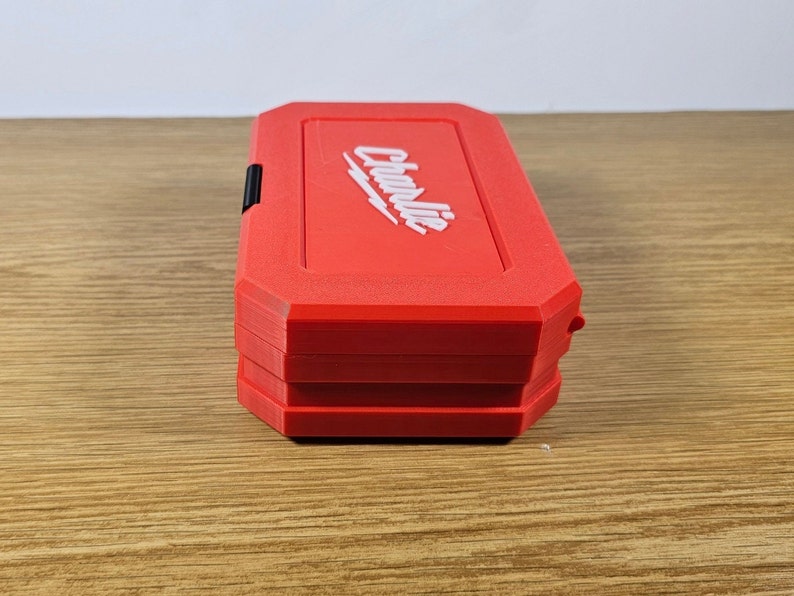 May include: A red tool box with the word "Charlie" printed in white on the top. The box is closed and has a black latch.