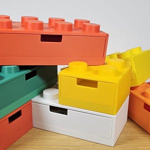 May include: A set of five colorful storage boxes with a drawer design. The boxes are made of plastic and have a lego-like appearance. The colors are orange, green, yellow, white, and orange.