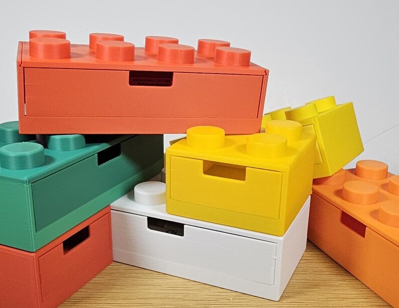 May include: A set of five colorful storage boxes with a drawer design. The boxes are made of plastic and have a lego-like appearance. The colors are orange, green, yellow, white, and orange.