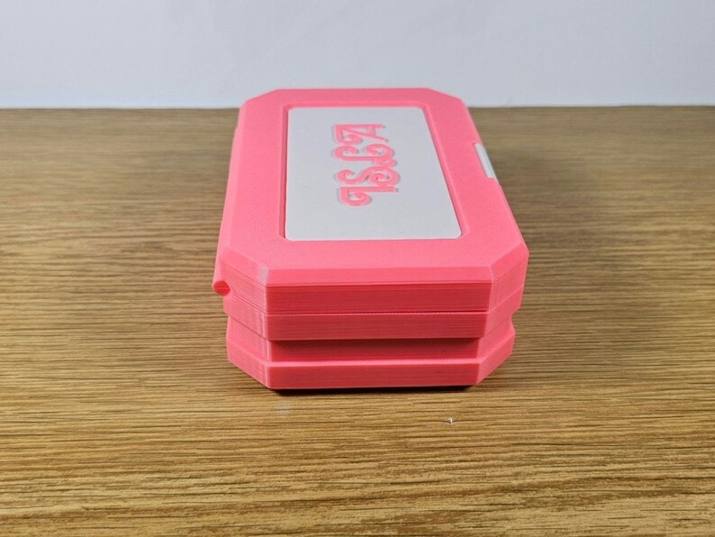 May include: A pink plastic case with the word "Aegis" printed on the top. The case is closed and has a white interior.