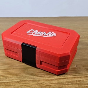 May include: A red plastic toolbox with a black latch and the word "Charlie" printed in white on the top.