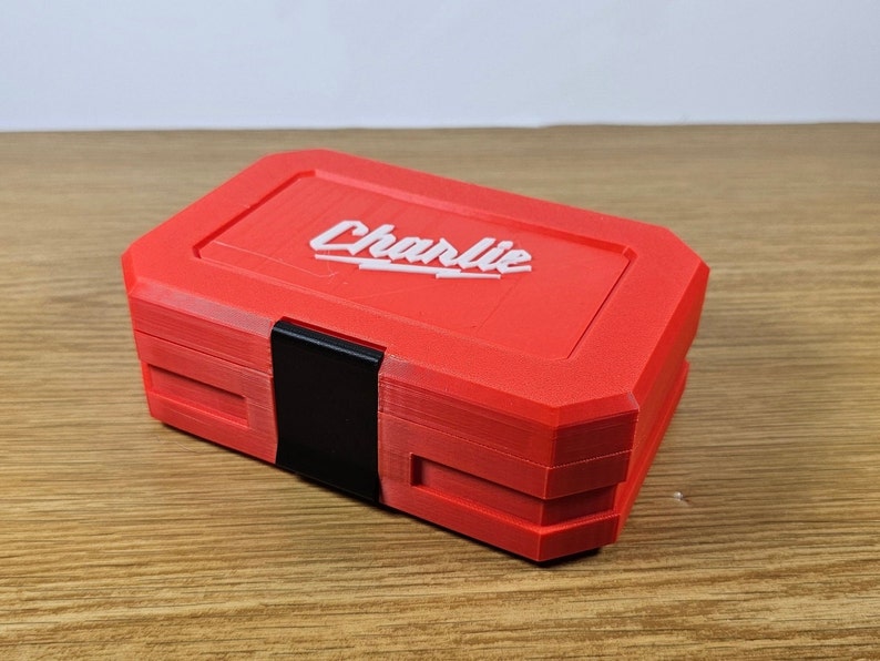 May include: A red plastic toolbox with a black latch and the word "Charlie" printed in white on the top.