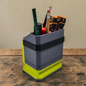 May include: A grey and neon green desk tidy containing pencils, pens, and small tools. The organiser has a geometric design with a black band around the middle. The base is neon green, and the top section is grey.