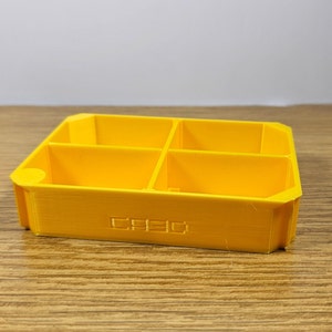 May include: A yellow plastic storage box with four compartments. The box has the word "CREO" printed on the bottom.